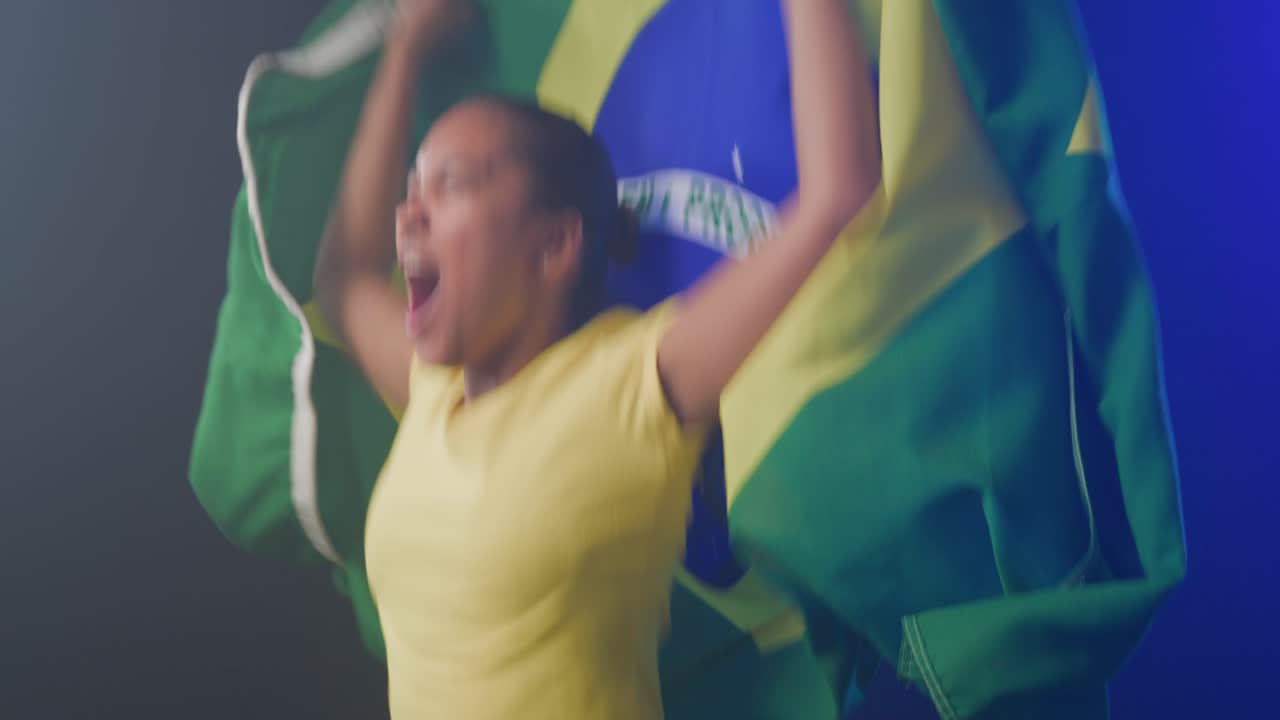 Donna afroamericana in studio dopo un'esultanza, che urla, sollevando una bandiera brasiliana e indossando una maglietta gialla