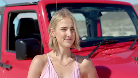 young caucasian woman poses by a red vehicle outdoors on a road trip