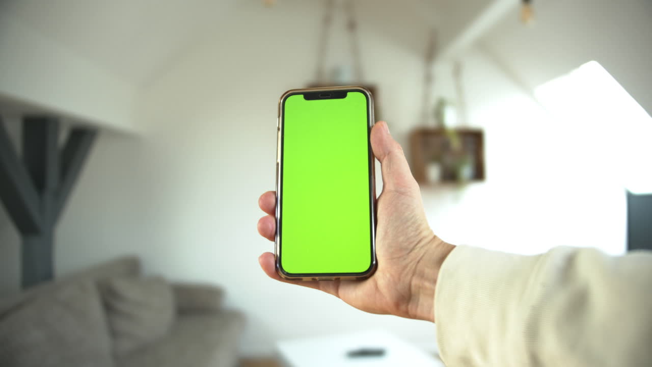 un punto de vista de un hombre sosteniendo un teléfono inteligente con pantalla verde en posición vertical en un fondo blanco aislado tocando el teléfono