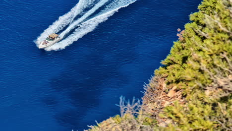 A-speedboat-races-through-the-deep-blue-waters-near-the-lush-cliffs-of-Navagio,-Greece