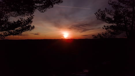 Aerial,-drone-shot,-flying-between-trees,-towards-the-sunset,-at-the-Dyblemyrheia-hill,-on-sunny,-autumn-day,-in-Lillesand,-Aust-Agder,-South-Norway