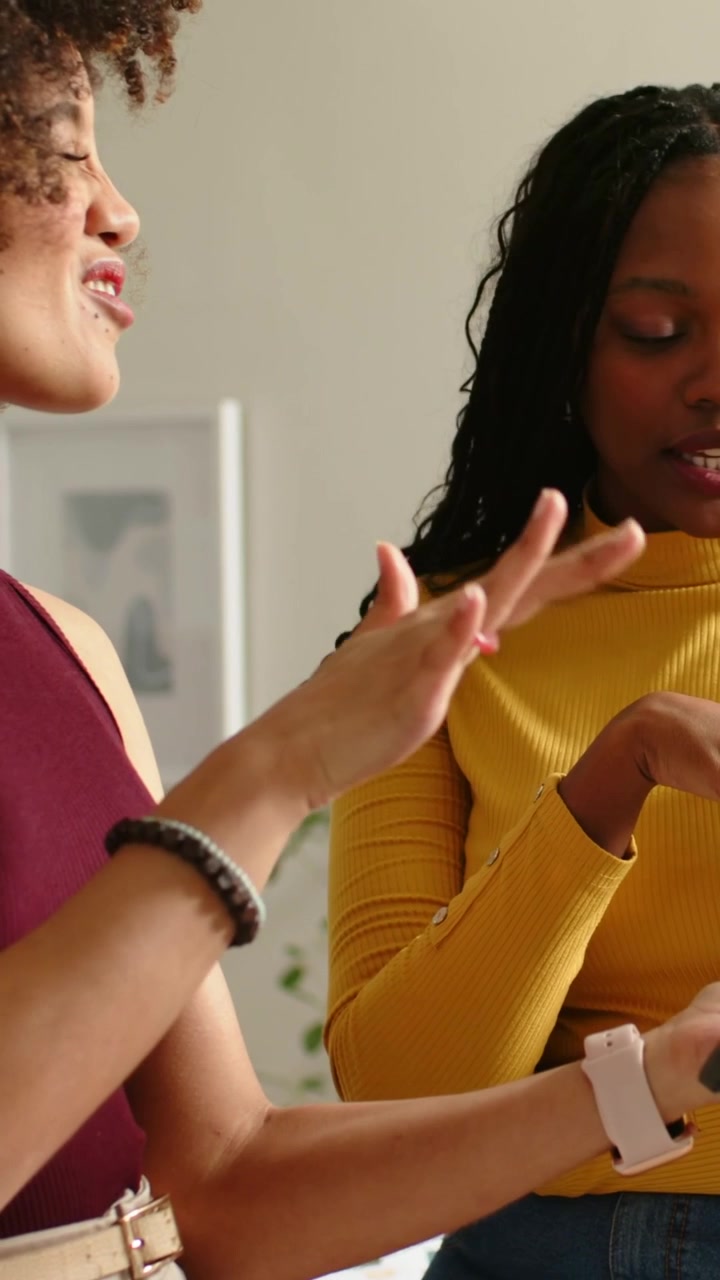 Vertical video: Starting left in maroon top discussing in home, right mustard checking phone, watch