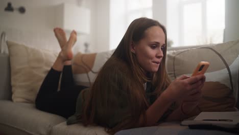mujer relajándose en un sofá, usando un teléfono inteligente