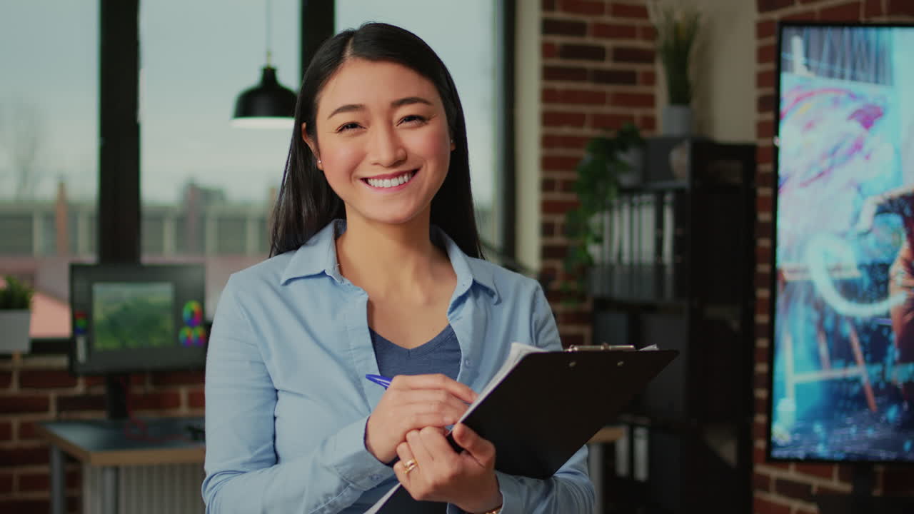 Happy asian woman taking notes on clipboard files in creative agency office