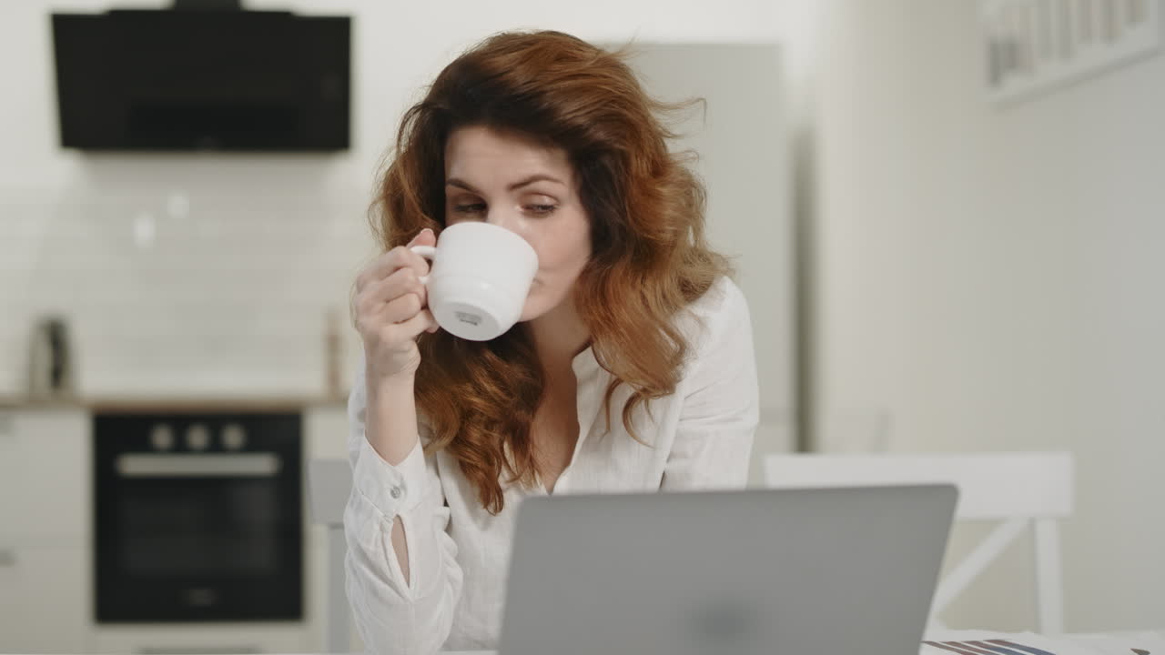 원격 작업장에서 노트북을 사용하는 행복한 여성. 집에서 차를 마시는 젊은 여성.