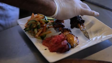 colocando pollo a la parrilla y kafta en un plato blanco junto a las verduras