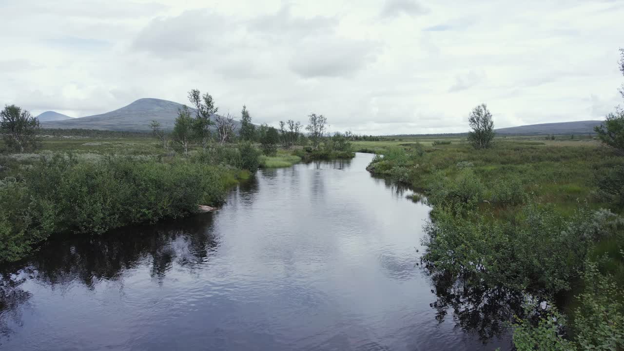 Rio tranquilo flui por planalto remoto da Noruega em dia ventoso.