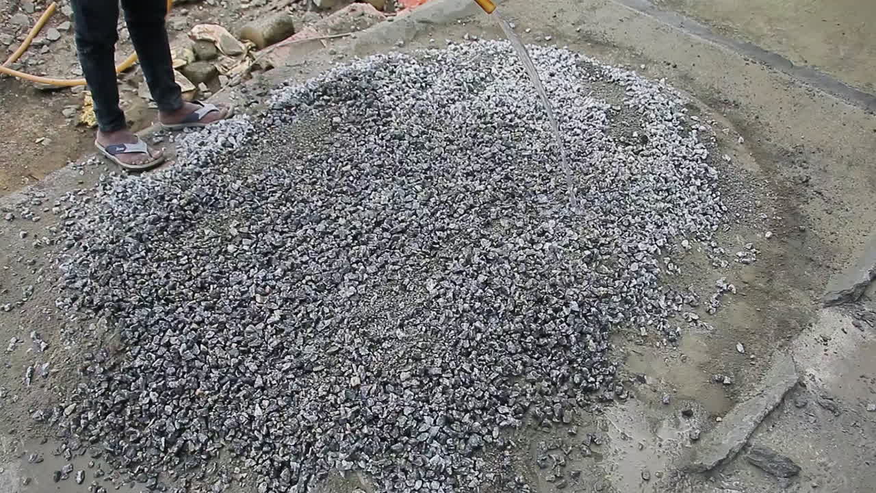 Indian mason worker pouring water over a pile of gravel mix to combine elements for construction