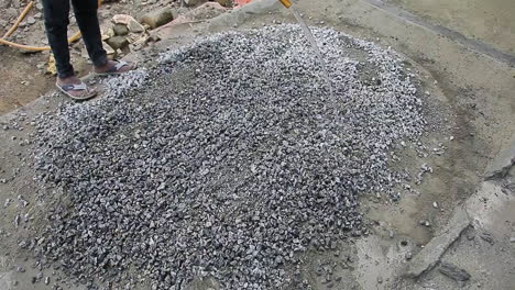indian mason worker pouring water over a pile of gravel mix to combine elements for construction