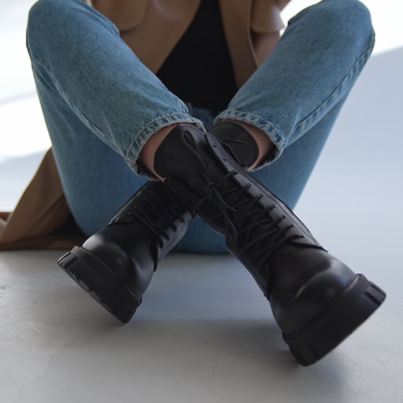 Female sits on the floor her stylish black boots near camera. Close up. Woman in jeans and coat showing her modern footwear