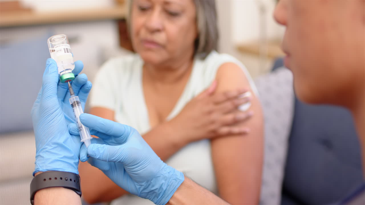 Preparing syringe, healthcare professional administering vaccine while senior woman waits