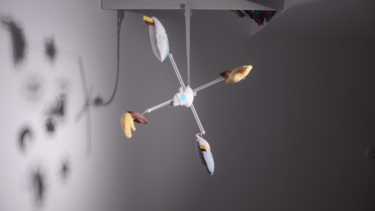 벽 배경에 있는 아기 침대 위에 매달려 회전하는 아기의 다채로운 모바일 장난감