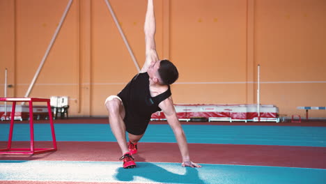 zoom en la toma de la cámara de un apuesto joven deportista calentándose y estirándose en una instalación deportiva cubierta