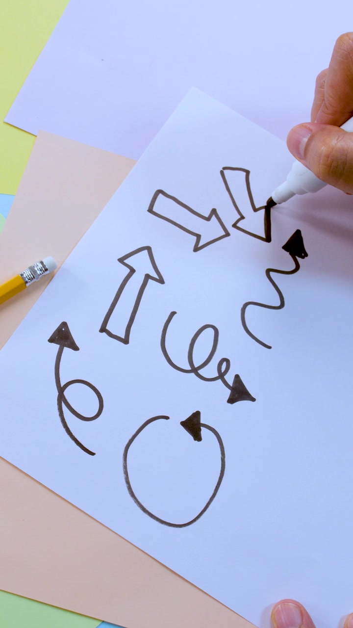 Person draws various arrows and squiggly lines on paper, overhead view, bright lighting