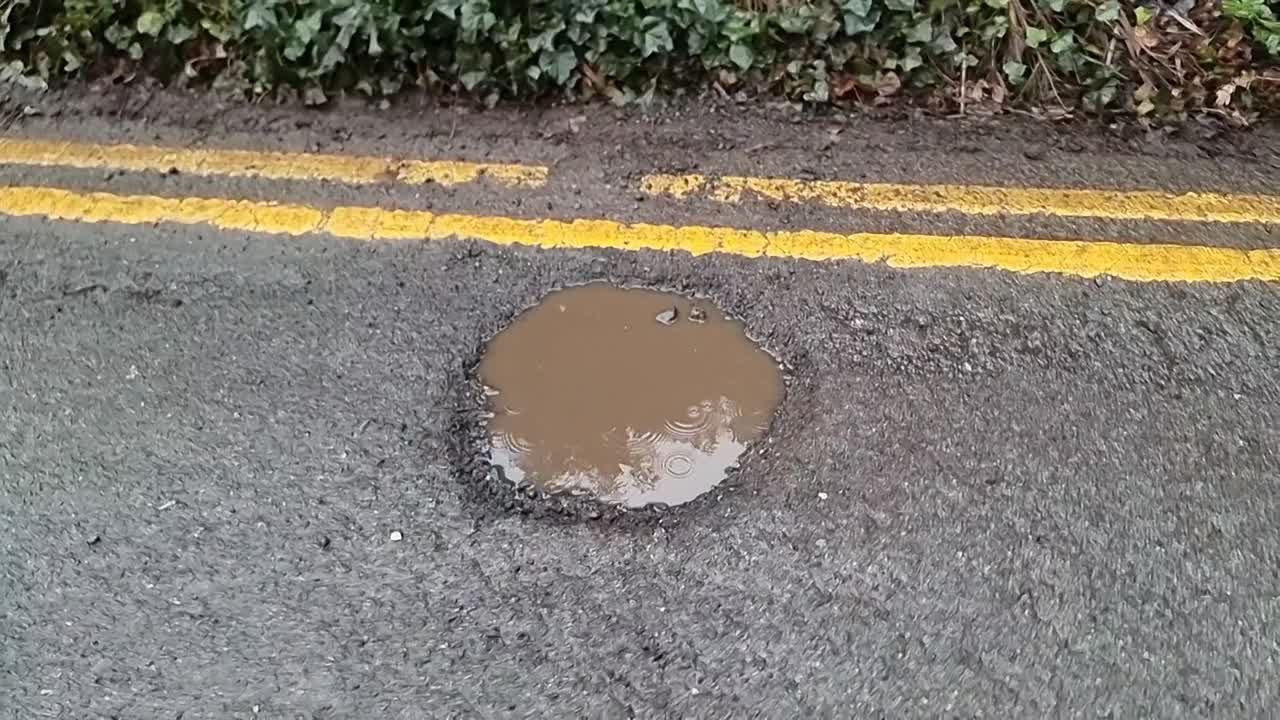 Road hazard double yellow lines with rain filled deep pot hole damaged tarmac asphalt surface