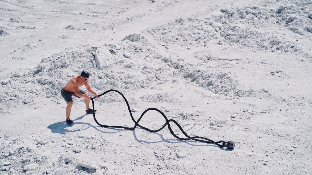 Athletic young man working out with battle ropes. Bodybuilder posing outdoors.