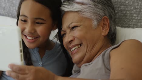 grandmother and granddaughter using digital tablet in bed room 4k