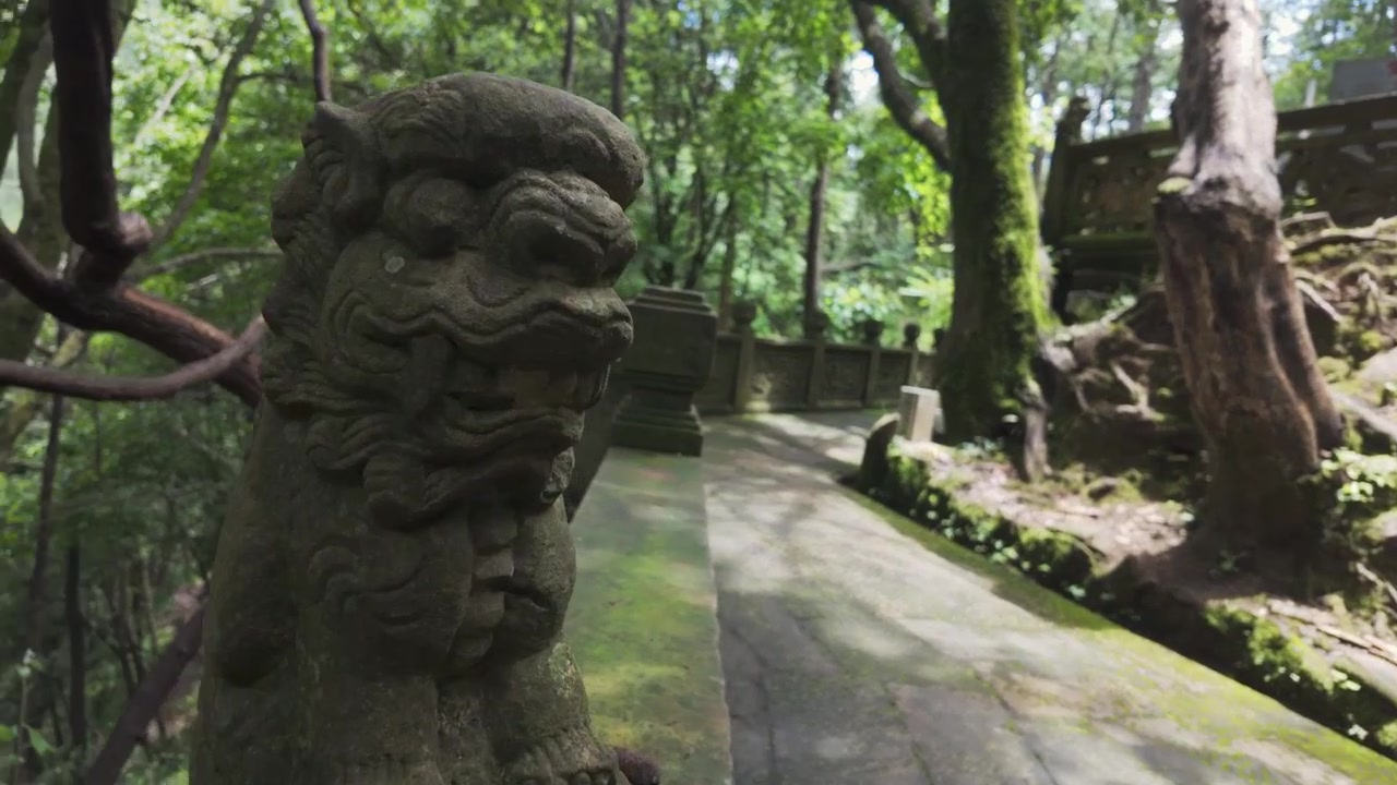 Una carrellata cinematografica rivela un'antica statua di leone in pietra che sorveglia un sentiero coperto di muschio in una serena foresta di montagna. Autentico patrimonio culturale e atmosfera di benessere.