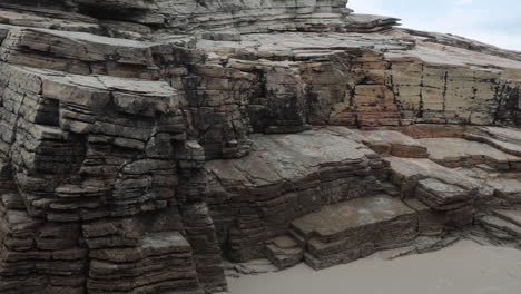 rocky sandstone cliffs with layered textures along a quiet beach under cloudy skies