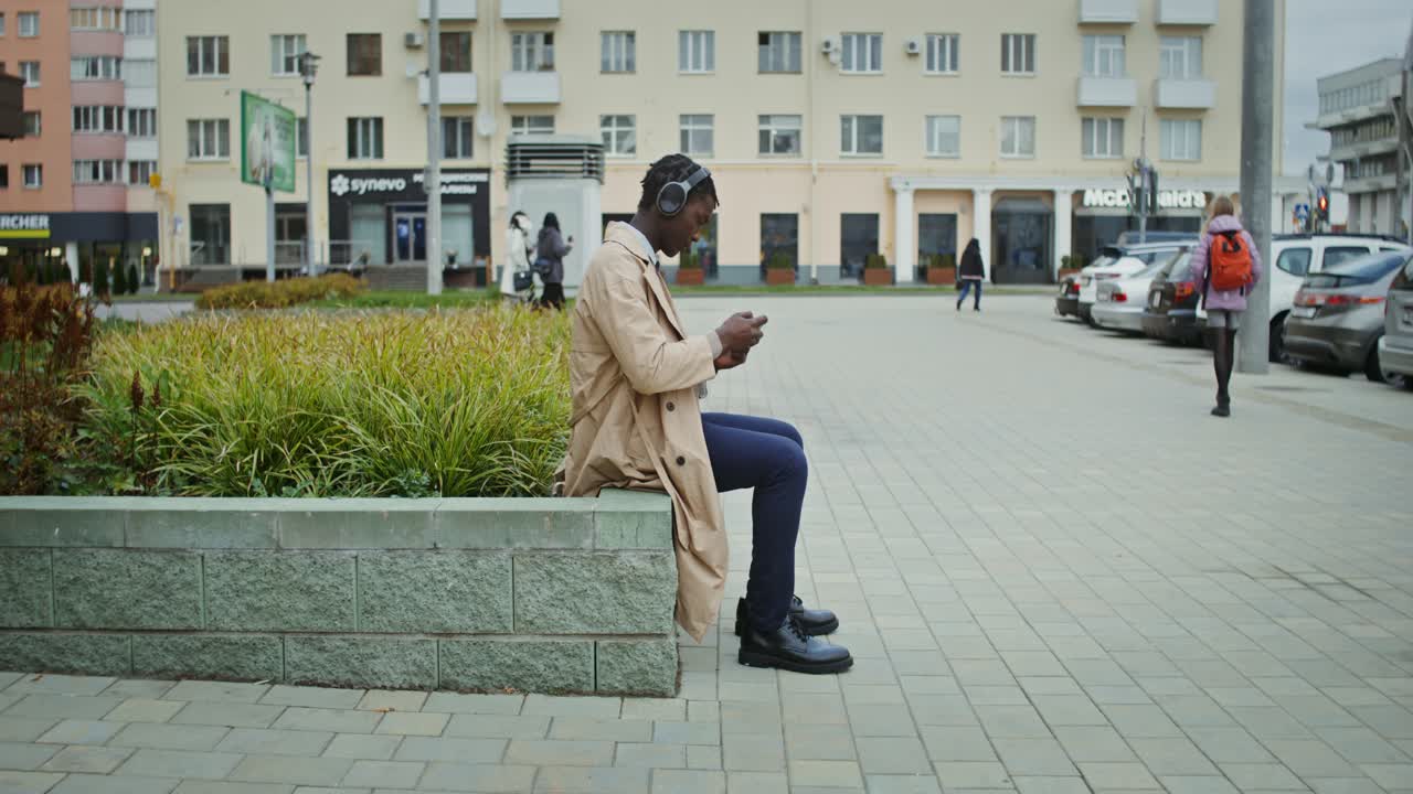 Man sitting on a bench in the city listening to headphones
