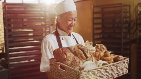 animation of happy asian female baker holding basket with diverse breads