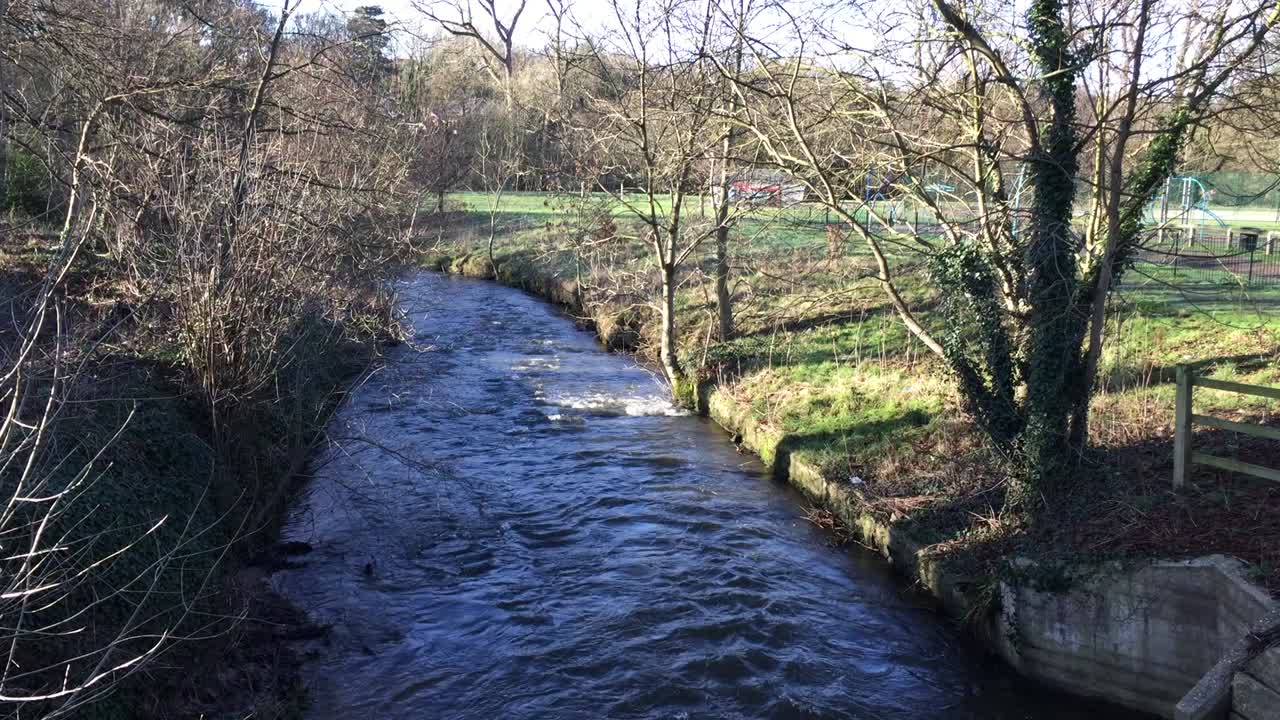 View of The River Bollin from the road bridge by St Bartholomew’s churchyard in Wilmslow, Cheshire, England, on a sunny winter’s day.
