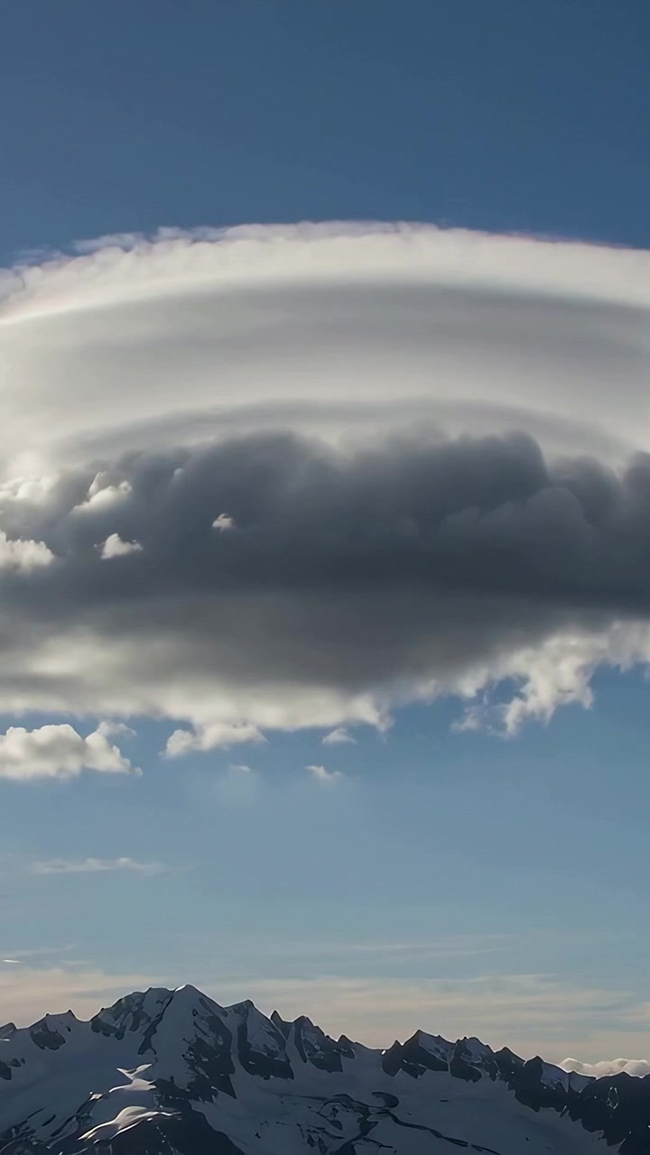 Vertical video: Panning shot revealing layered lenticular cloud above ridge, revealing snowy peaks