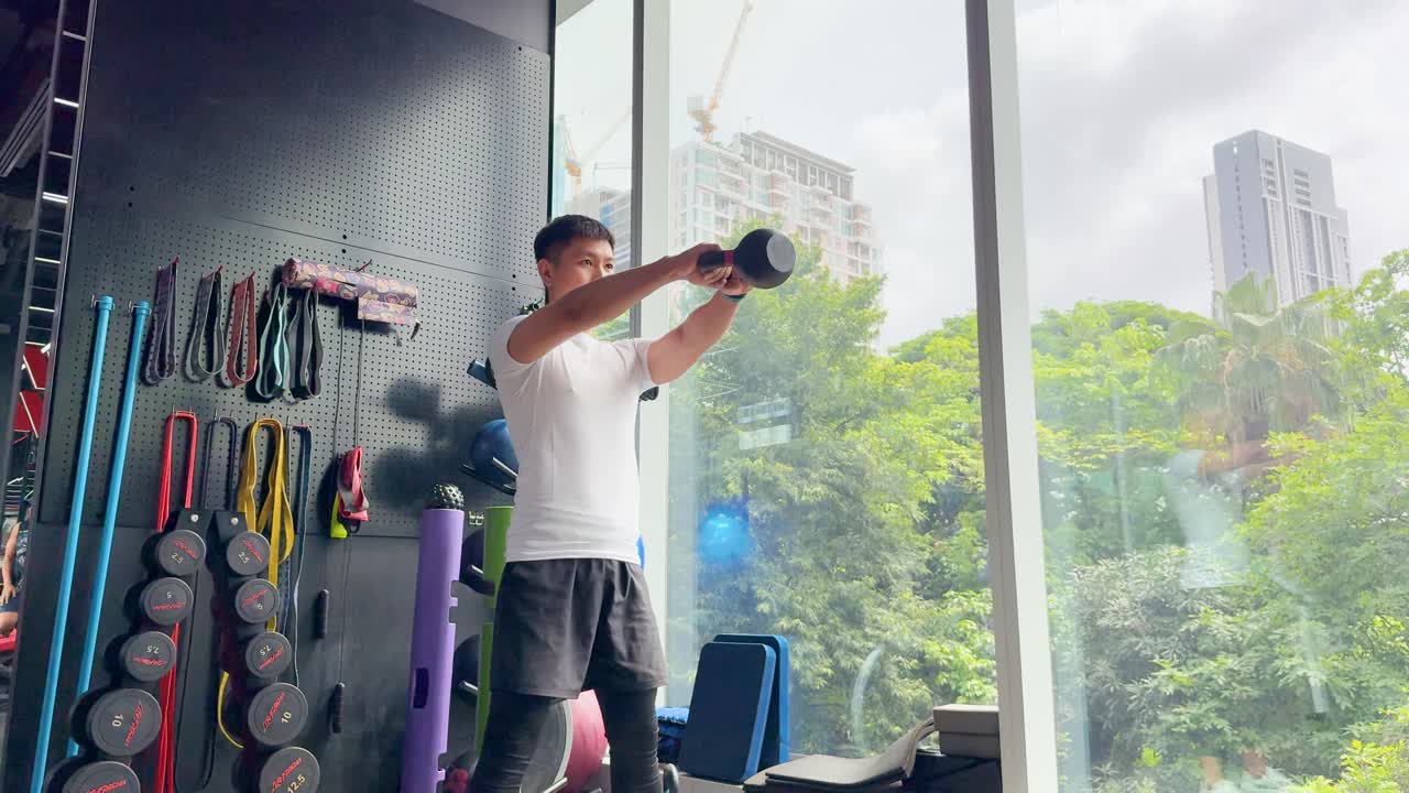 Two men perform kettlebell exercises in a bright, spacious gym with large windows and city views