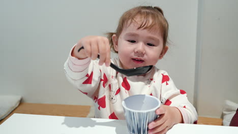 young asian toddler drinks water from mug using chirirenge, japanese soup spoon