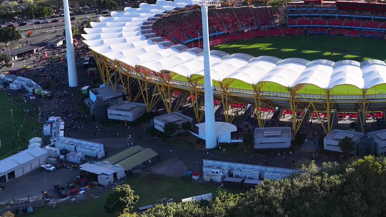 High-angle drone shot of a large sports arena under bright sunlight with white canopy architecture.