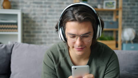young man relaxing on couch, listening to music and using smartphone