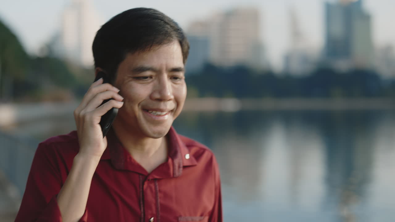 Man talking on a phone in a city park near a lake