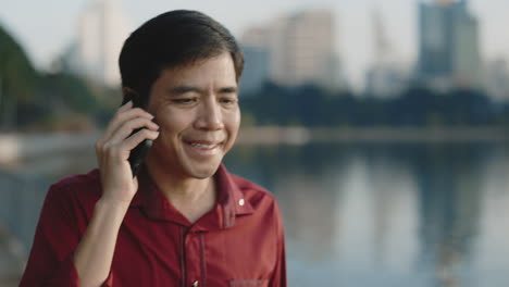 man talking on a phone in a city park near a lake