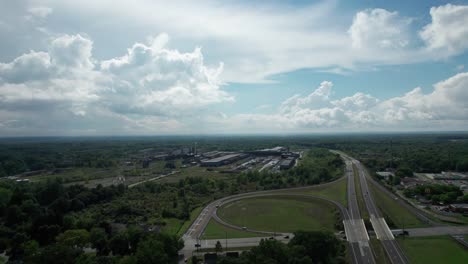 Drohne-Macht-Luftaufnahmen-Einer-Kleinen-Stadt,-Einer-Autobahnkreuzungskreisstraße-In-Einem-Bewölkten-Blauen-Himmel