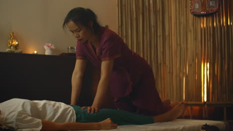 an asian woman performs a traditional thai massage on the back of a lying beautiful european girl. chiropractor produces treatment with alternative methods.