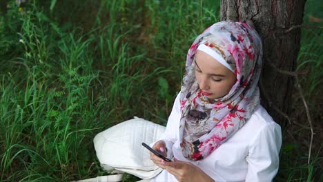 young woman in hijab using smartphone outdoors