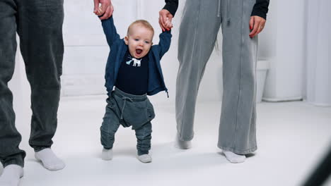 little cute baby making slow steps and smiling adorably. parents hold their son by the hands.