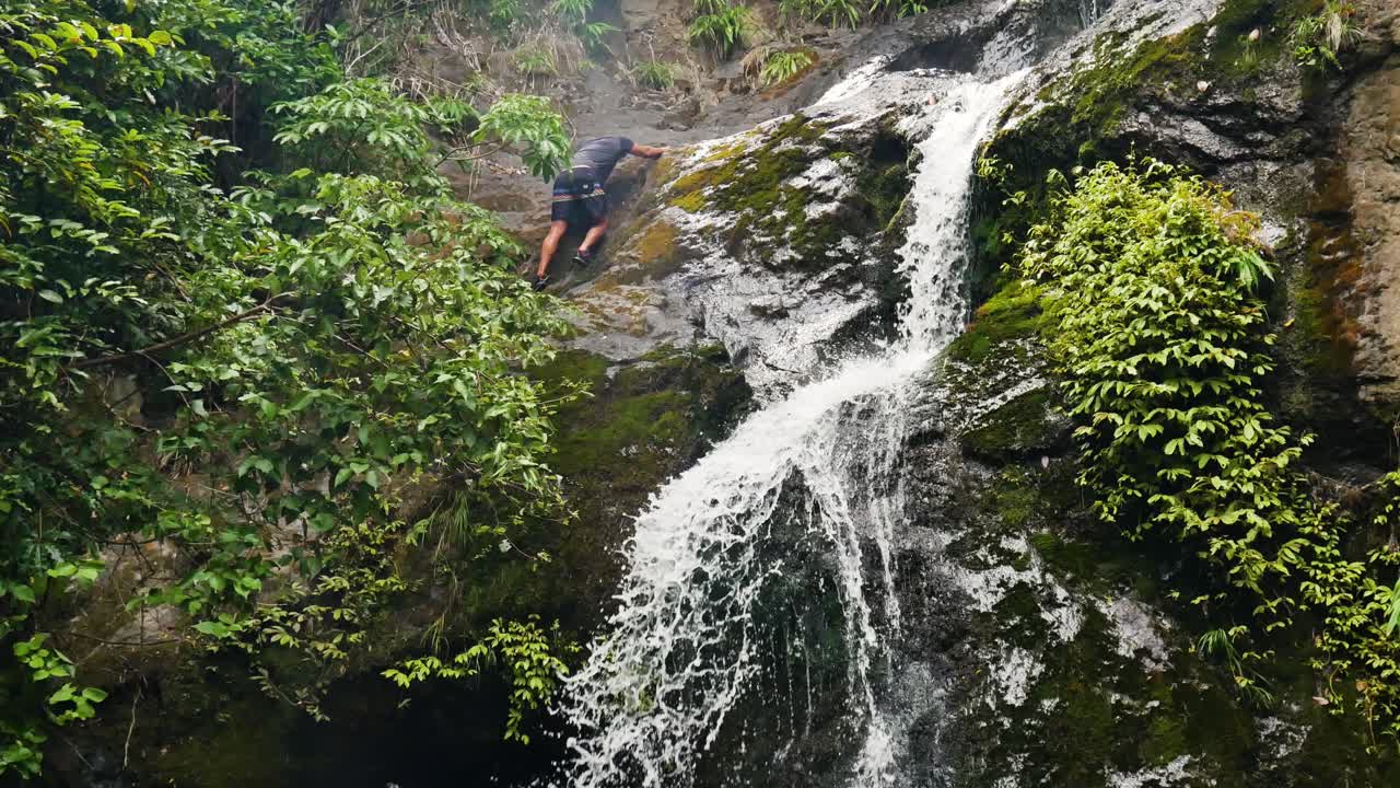 hiker downclimbs slippery jungle waterfall