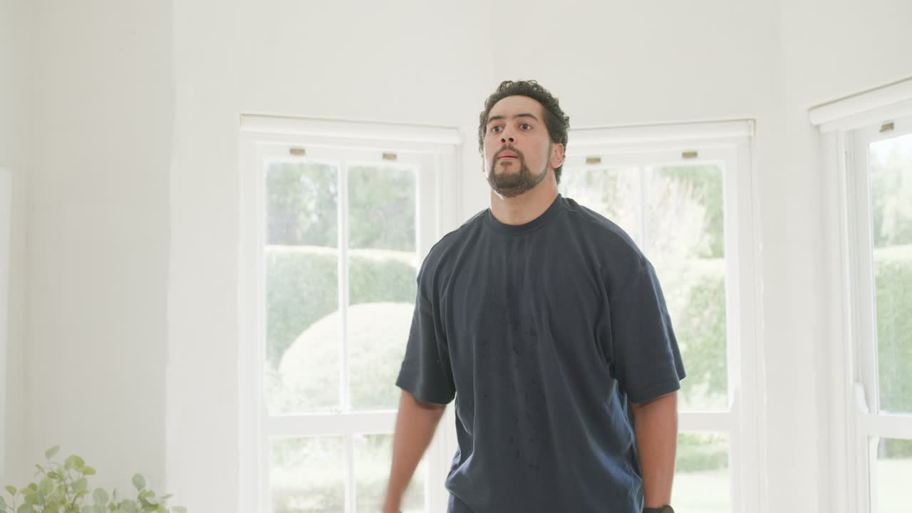 出窓のそばで、ネイビーのTシャツを着たアフリカ系アメリカ人男性が、六角形のウェイトを持ち、筋肉を引き締めるためにフロントレイズとサイドレイズを行っている。
