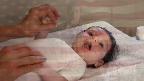 Animation-of-flag-of-usa-waving-over-hands-of-biracial-mother-playing-with-baby
