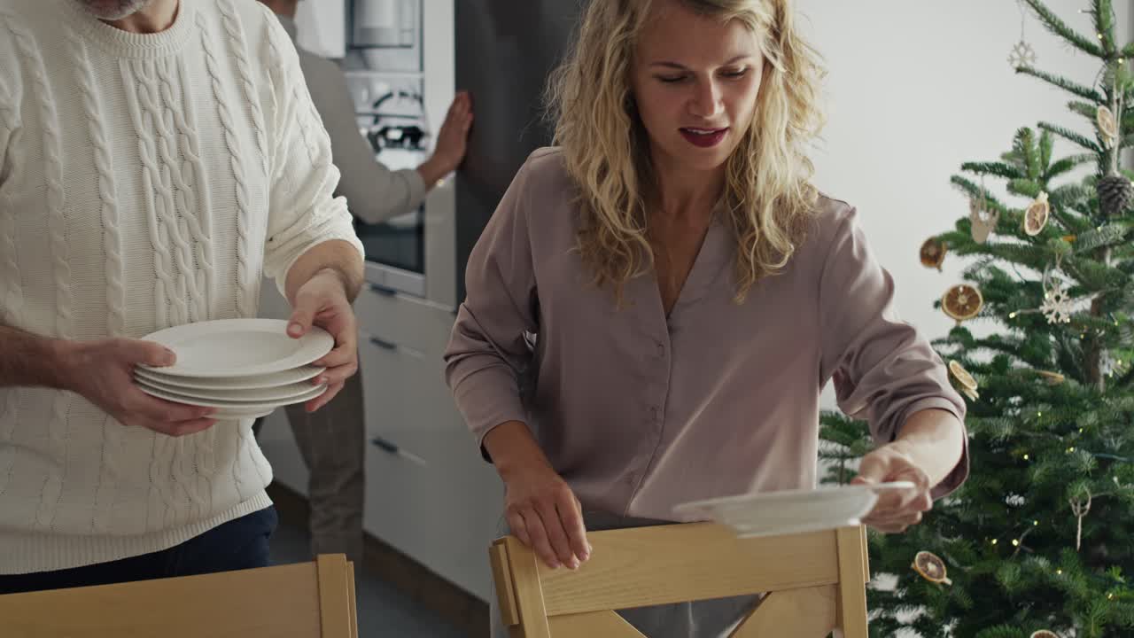 큰 백인 가족이 크리스마스 이브에 테이블을 준비하고 있습니다.