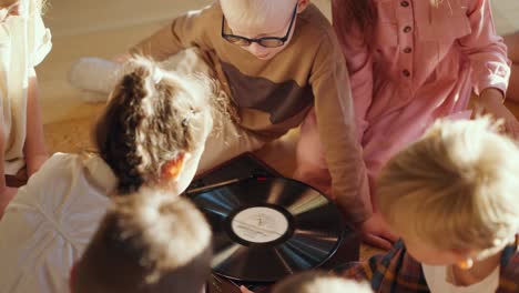 close-up shot of preschool children sitting after the record player looking at it and listening to music. the children learn music