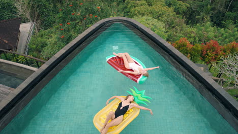 two women floating in swimming pool lying on inflatables best friends having fun summer day on vacation at tropical hotel resort wearing bikinis top view