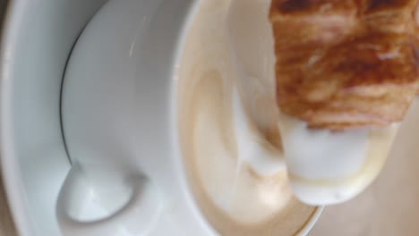 croissant dipping into a latte with latte art