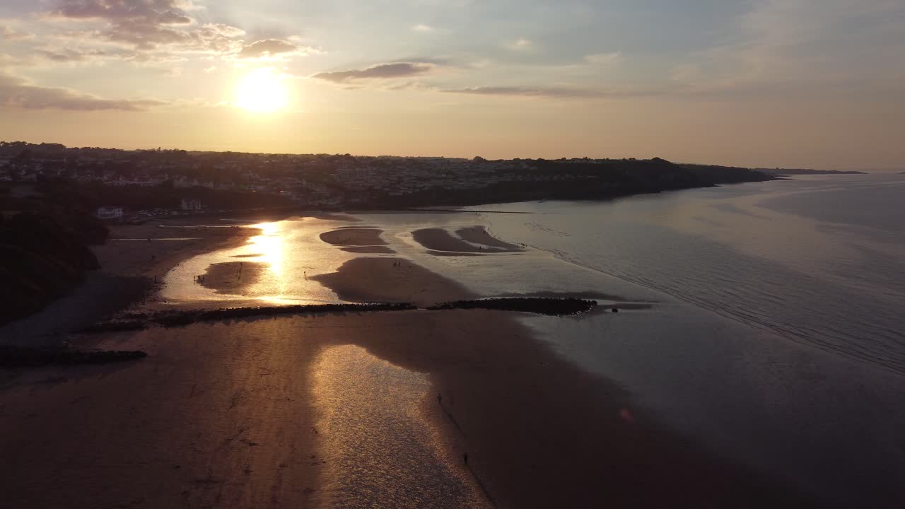 Raggi del tramonto irradiano colori dorati e infuocati su una rilassante costa oceanica, vista aerea con lento movimento in avanti e a sinistra.