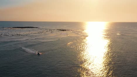 aerial pullback shot of jet ski riding on ocean during beautiful sunrise, sun rays reflecting off water in sydney, australia