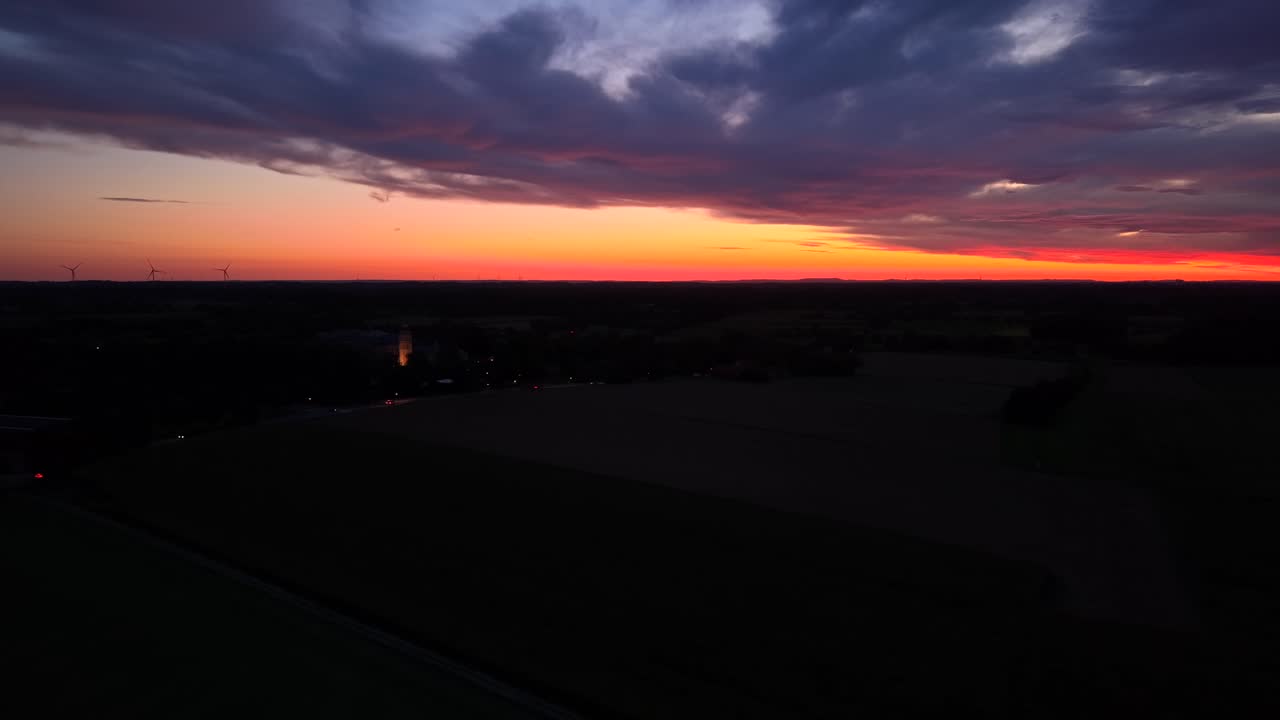 Oranje verlichte lucht bij zonsopgang met dramatische wolken in de VS. Brede luchtfoto. Verlichte kerktoren in een buitenwijk. Vredige ochtend in Amerika. Windturbine op de achtergrond