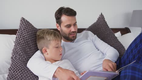padre e hijo acostados en la cama y leyendo un libro de cuentos en el dormitorio en casa 4k