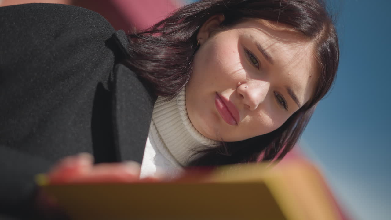 dama sentada pensativa al aire libre, iluminada por la luz del sol, el cabello balanceándose suavemente en el viento, centrada en el libro en su mano con una luz suave acentuando su concentración