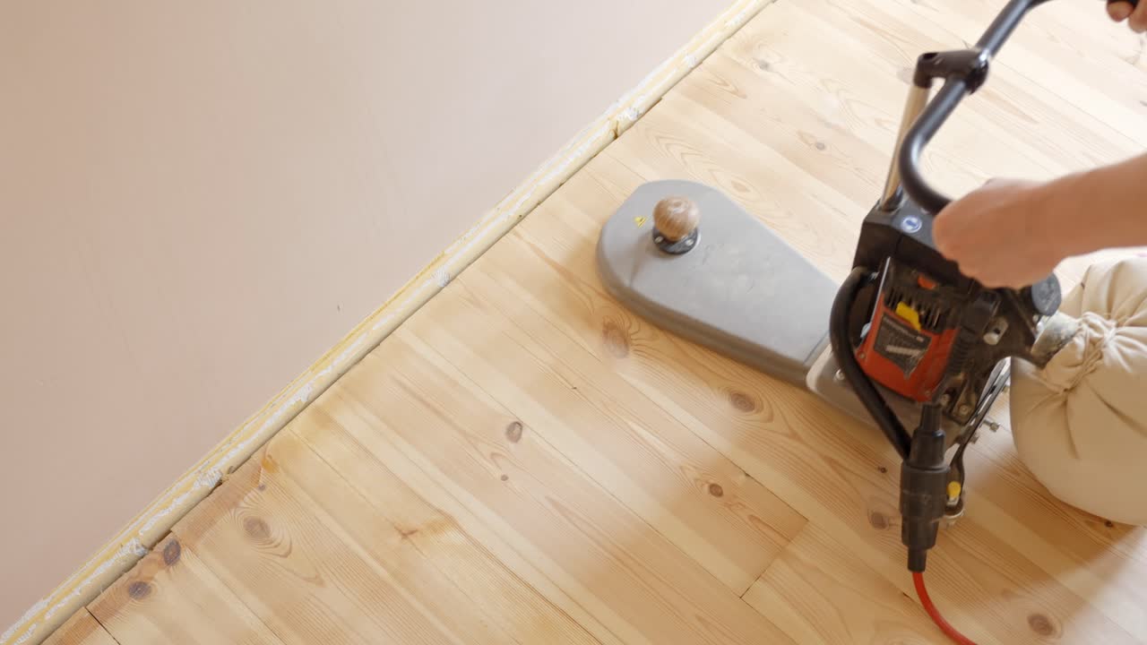 A close-up view of sanding the edges of a wooden floor, preparing it for finishing or polishing